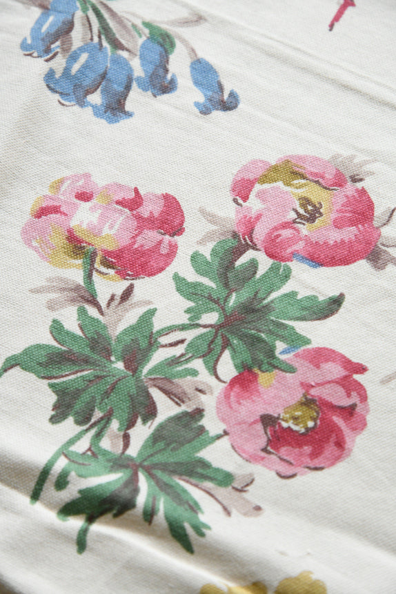 Close view of pink and blue floral motifs across cream vintage textile